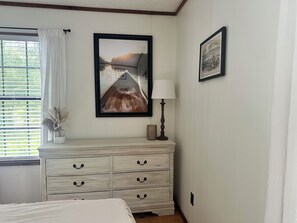 A bedroom with a bed, a dresser with drawers, a lamp, and two framed pictures on the wall.