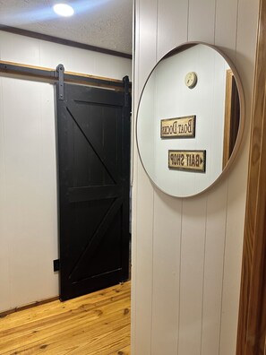 A room with a black sliding barn door, a circular mirror with a wooden frame, and a wooden floor.