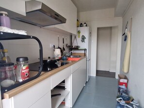 Eine Küche mit Herd, Spüle und diversen Küchengeräten. Ein Kühlschrank und ein Fenster mit Vorhängen sind ebenfalls vorhanden.