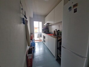 A narrow kitchen with white cabinets, a refrigerator, and a window providing natural light.