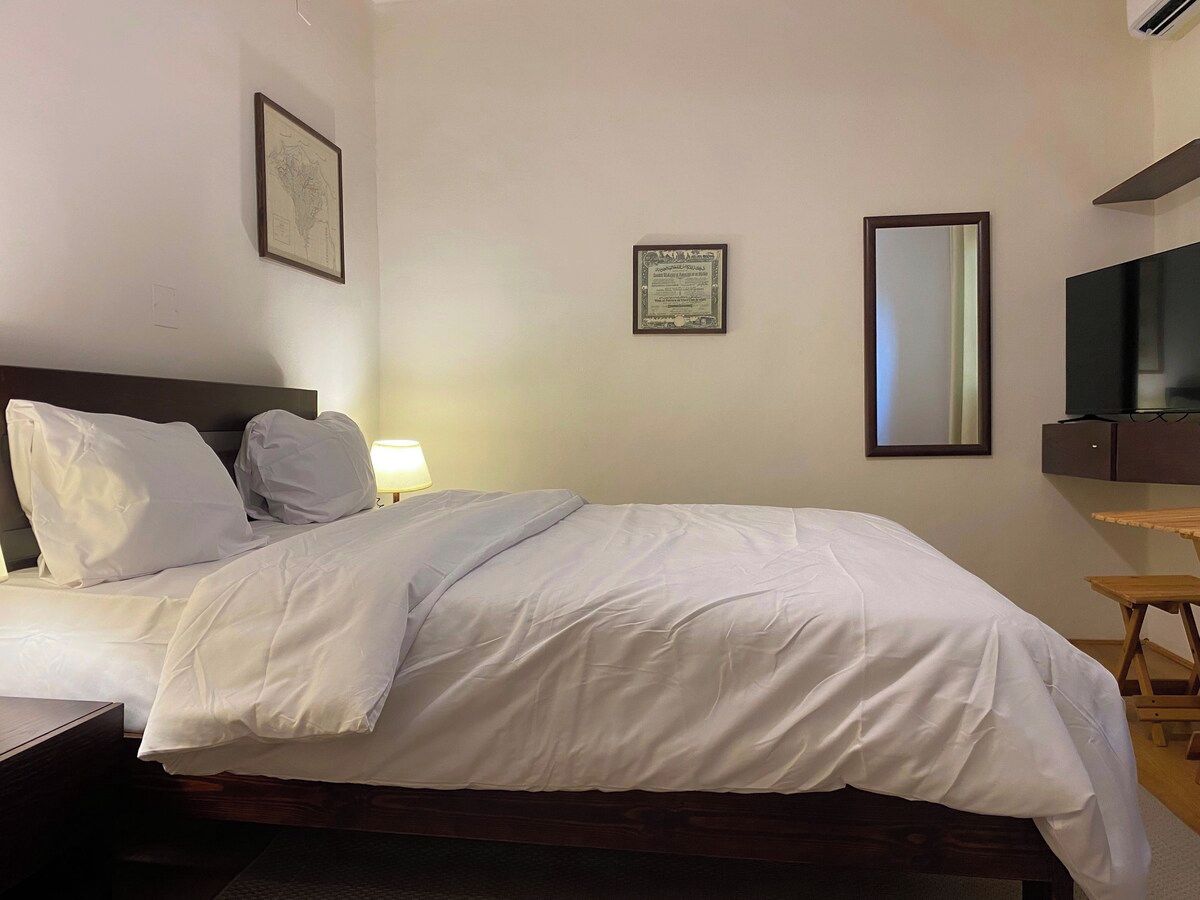 Une chambre d’hôtel avec un lit, un bureau, une chaise, une télévision et un certificat encadré accroché au mur.