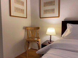 Ein Hotelzimmer mit Bett, Sessel, Nachttisch mit Lampe und gerahmten Bildern an der Wand.