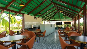 Un espace de restauration intérieur avec des tables rondes et des chaises orange, un sol carrelé et une structure de toit végétalisée.