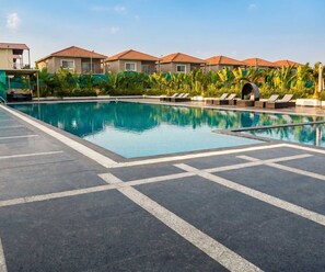 A swimming pool with lounge chairs and a covered seating area, surrounded by buildings with red roofs.