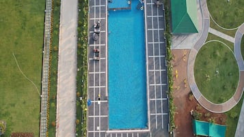 An aerial view of a swimming pool with a surrounding deck area, including a parking lot and landscaped gardens.