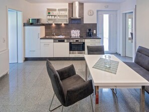 A modern kitchen with white cabinetry, a built-in oven, and a dining area with a white table and two chairs. - Holiday Apartment With 1 Bedroom (Esens)