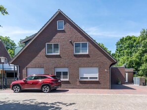 Ein rotes Auto parkt vor einem Ziegelhaus mit einer Garagentür, einem kleinen Fenster und der Hausnummer 9.