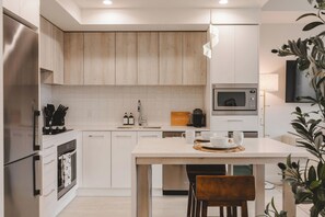 A modern kitchen with white cabinetry, a central island, a built-in microwave, and a hanging light fixture.