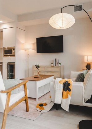 A modern living room with a flat-screen TV, a wooden side table, a white sofa, and a floor lamp.