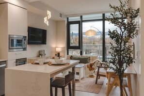 A modern kitchen with a dining area, large windows, and a view of the outdoors.