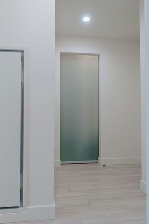 A hallway with a door, a light fixture on the ceiling, and a wooden floor.