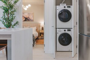 A compact living space with a kitchenette, a bed, and a wall-mounted washer-dryer unit.