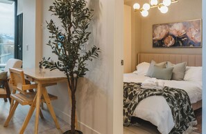 A room with a bed, a painting, and a potted plant.