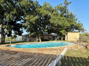A swimming pool with a tiled edge, surrounded by a grassy area and trees. - Fredericksburg Getaway with Private Pool (Fredericksburg)