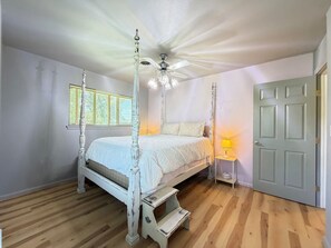 Ein Himmelbett mit Deckenventilator, einer Nachttischlampe und einem Fenster mit Jalousien.
