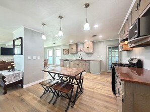 A modern kitchen with wooden cabinets, a central island, pendant lighting, and a dining area with a wooden table and chairs. - Fredericksburg Getaway with Private Pool (Fredericksburg)