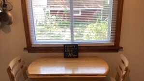 Una pequeña mesa de madera con un cartel que dice 'Siempre hay tiempo para una copa de vino' en una habitación con una ventana y una silla blanca.