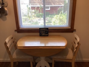 Uma pequena mesa de madeira com uma placa que diz 'Sempre há tempo para um copo de vinho' em um quarto com janela e uma cadeira branca.