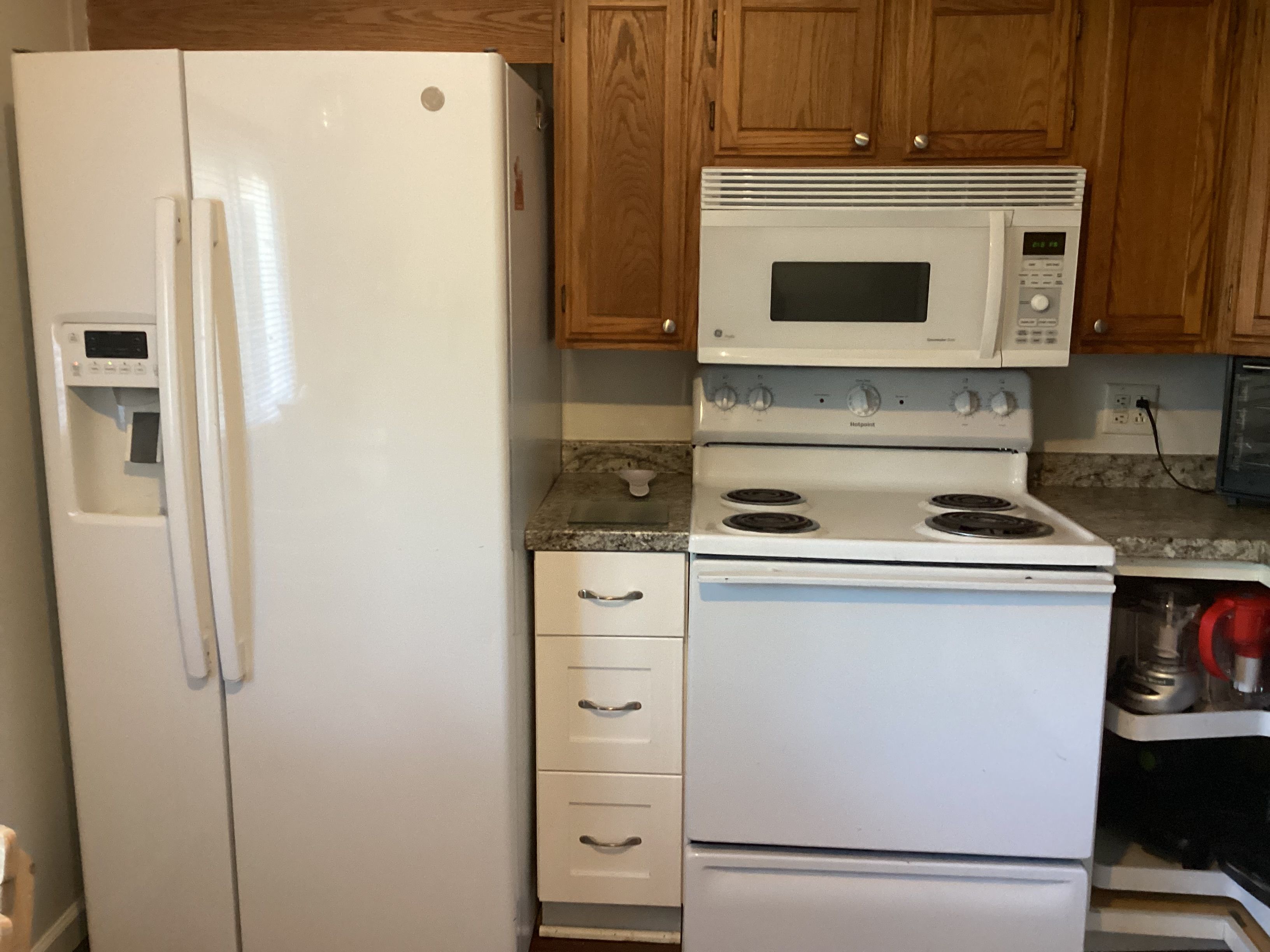 Une cuisine avec un réfrigérateur blanc, un four à micro-ondes, une cuisinière et des armoires en bois.