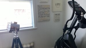 Una habitación con una bicicleta estática, un trípode con una cámara y citas motivacionales en la pared.