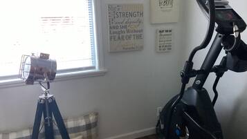 Una stanza con una cyclette, un treppiede con una fotocamera e citazioni motivazionali alle pareti.
