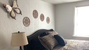 Un dormitorio con una cama, una lámpara, una cesta y elementos decorativos en la pared.