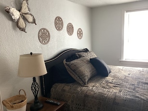 Quarto com cama, abajur, cesta e detalhes decorativos na parede.