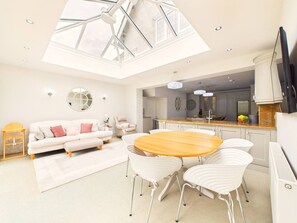 A modern living room with a dining area, a sofa, a coffee table, and a TV. - Cheltenham Retreat | Luxury | Garden | Sleeps 11 (Charlton Kings)