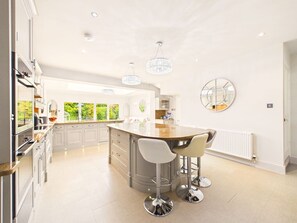 A modern kitchen with a central island, bar stools, and a large window providing natural light. - Cheltenham Retreat | Luxury | Garden | Sleeps 11 (Charlton Kings)