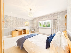 A bedroom with a bed, bedside tables, a dresser, a window with curtains, and a chandelier. - Cheltenham Retreat | Luxury | Garden | Sleeps 11 (Charlton Kings)