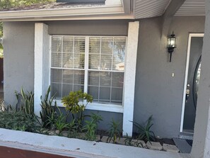 A house with a large window, a door with a light fixture, and a small garden with various plants. -     Tampa Zen Retreat Private Pool, Tiki Bar & 4BR Home (Tampa)