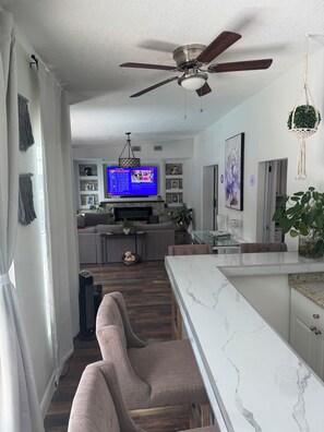 A modern kitchen with a marble countertop, a ceiling fan, and a television in the background. -     Tampa Zen Retreat Private Pool, Tiki Bar & 4BR Home (Tampa)