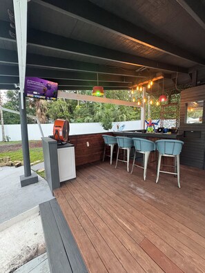 Eine Außenpatio mit Holzterrasse, Grill und Barbereich mit Stühlen.