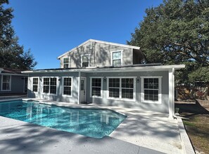 Una casa de dos pisos amb piscina, finestres grans i una zona de porxo coberta.