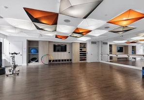 Una habitación amplia con piso de madera, un espejo grande y un techo con lámparas geométricas.