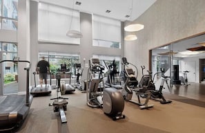 A gym with various cardio machines, large windows, and a high ceiling.