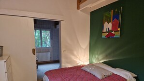Ein Schlafzimmer mit einem Bett, einem Bild, einem Fenster und einer Tür zu einem anderen Raum.