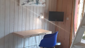 Ein Zimmer mit einem Holztisch, einem blauen Stuhl, einem Bild an der Wand und einem Fernseher.