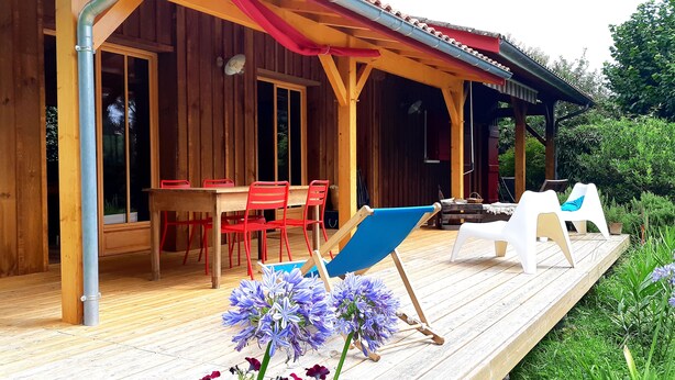 Eine Holzterrasse mit Tisch und Stühlen, umgeben von Kübelpflanzen und Blumen.