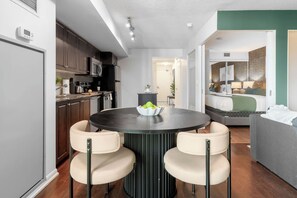 A modern kitchen with dark cabinets, a round dining table with two chairs, and a bowl of fruit on the table.
