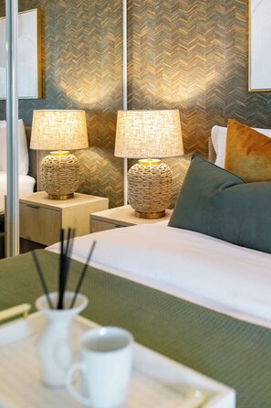 Une chambre d’hôtel avec un lit, deux lampes de chevet, une table de chevet, un plateau avec une tasse et un porte-bougie, et un mur à texture.