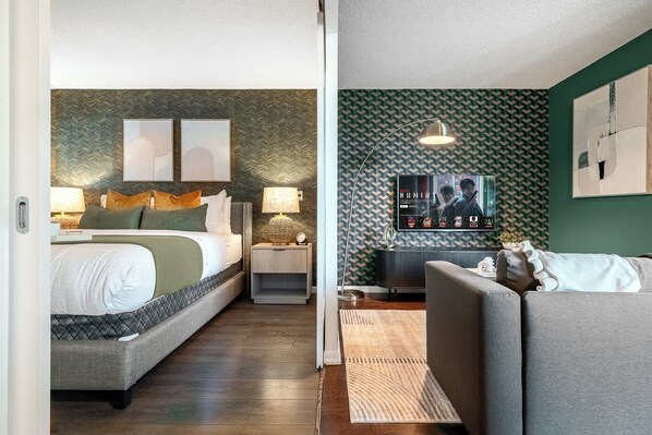 A hotel room with a bed, nightstand, lamp, and a sofa.