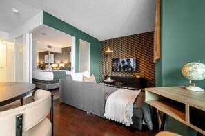 A modern living room with a sofa, a dining table, and a TV mounted on the wall. - Bright Fort York 1BR Private Balcony & Lake! (Toronto)