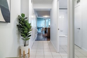 A hallway with a potted plant, a door, and a glimpse of a dining area with a table and chairs.