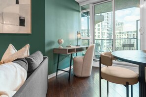 A modern living room with a green accent wall, a round dining table, and a view of the cityscape through large windows.