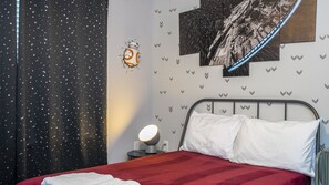 Ein Schlafzimmer mit einem Bett, einem Nachttisch mit Lampe, einer Wand mit Sternenmuster-Tapete und einem Poster.