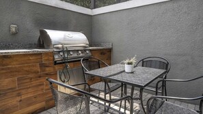 Eine Terrasse im Freien mit Grill, Tisch und Stühlen.