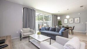 A modern living room with a sofa, armchairs, a coffee table, and a dining area with a table and chairs. - 4BR Le Reve Resort Pool Near Disney & Universal (Kissimmee)