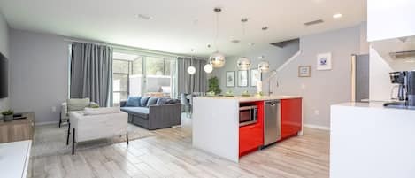 A modern living room with a sofa, a dining area with a red island, and a kitchen with a microwave.