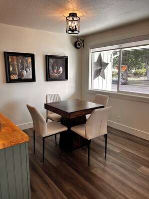 Un comedor con una mesa y sillas de madera, una obra de arte enmarcada en la pared y un ventanal decorado con estrellas.